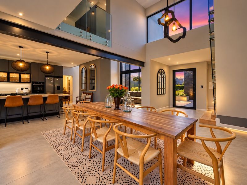 Spacious open-plan living and dining area featuring a modern kitchen with island, double-volume ceilings, and a sleek staircase with glass balustrade.