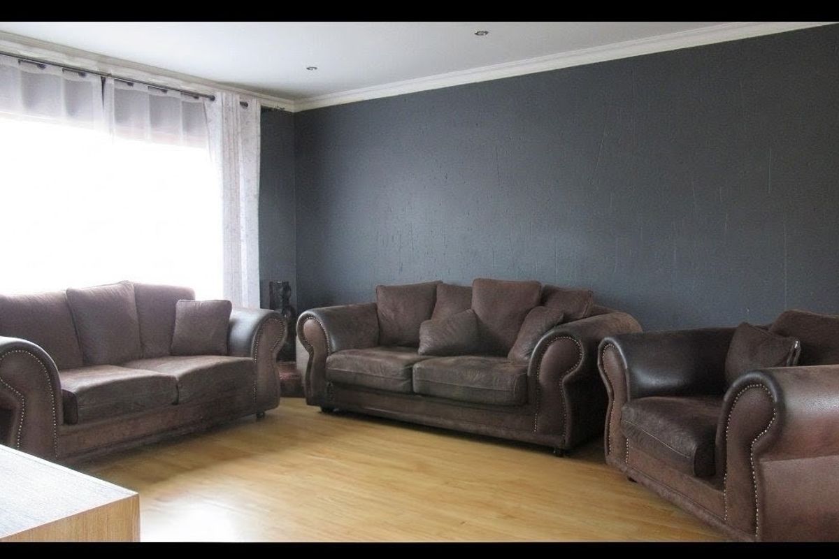 A living room featuring laminate flooring, recessed downlights, and a dark accent wall with coved ceiling cornicing.