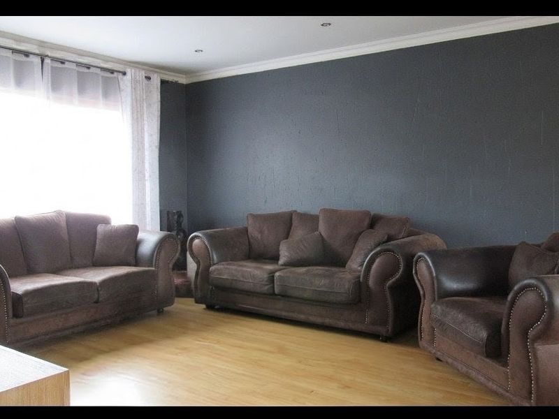 A living room featuring laminate flooring, recessed downlights, and a dark accent wall with coved ceiling cornicing.