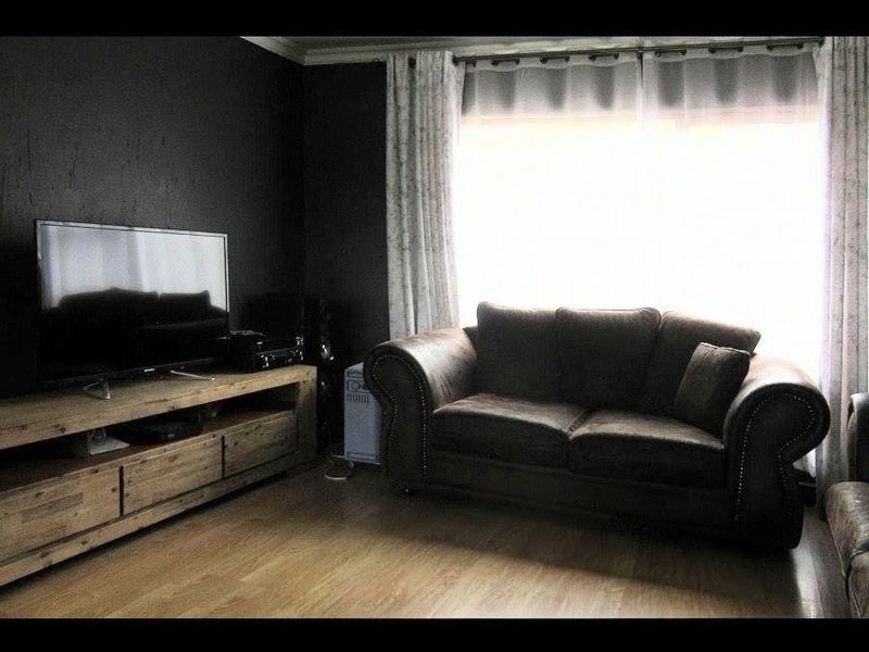 A living room featuring dark painted walls, laminate flooring, and crown molding, with natural light entering through a large window.