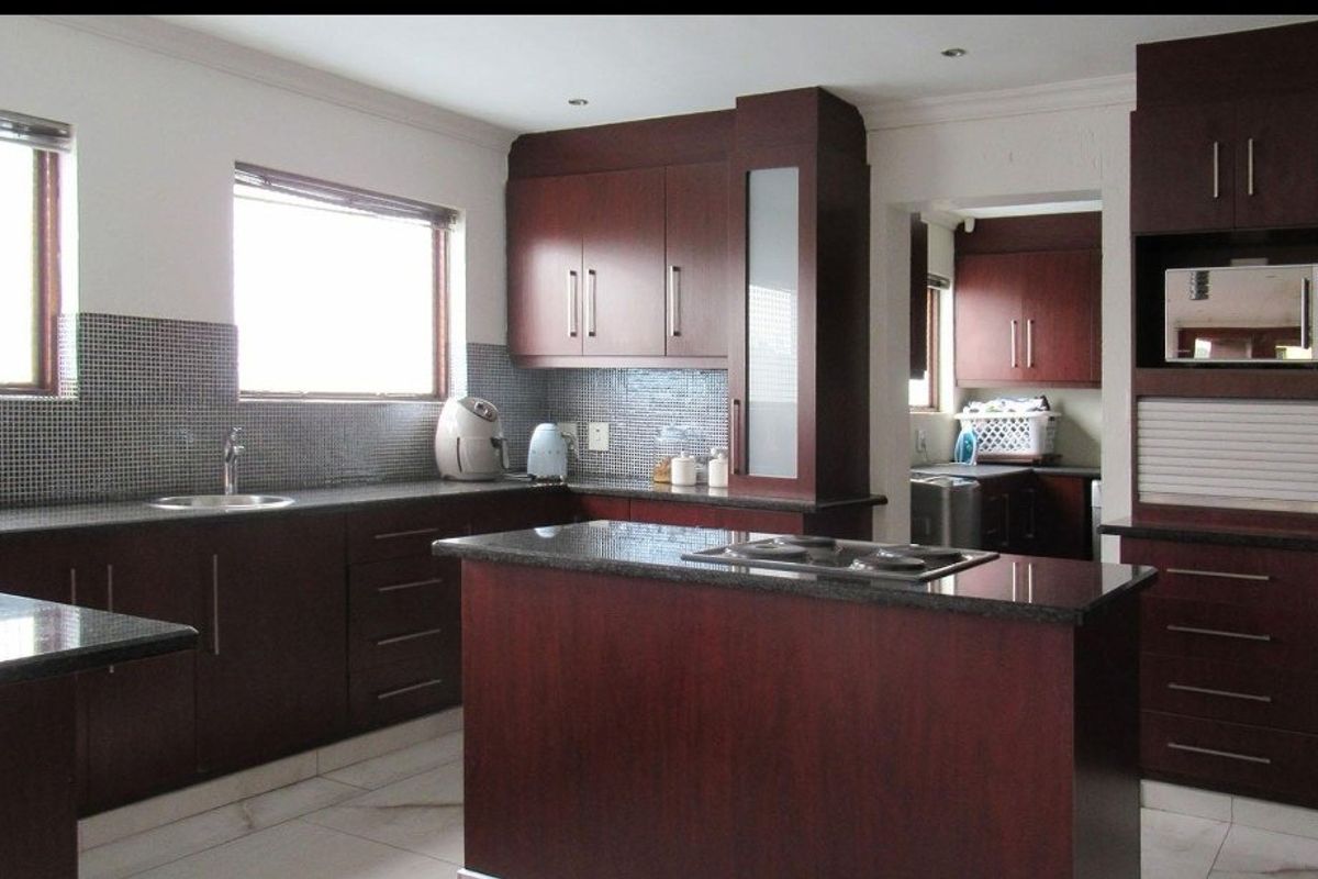 A functional kitchen featuring dark wood cabinetry, granite countertops, a central island with a cooktop, and a mosaic tile backsplash.