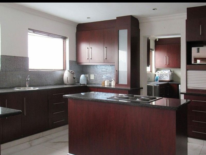 A functional kitchen featuring dark wood cabinetry, granite countertops, a central island with a cooktop, and a mosaic tile backsplash.