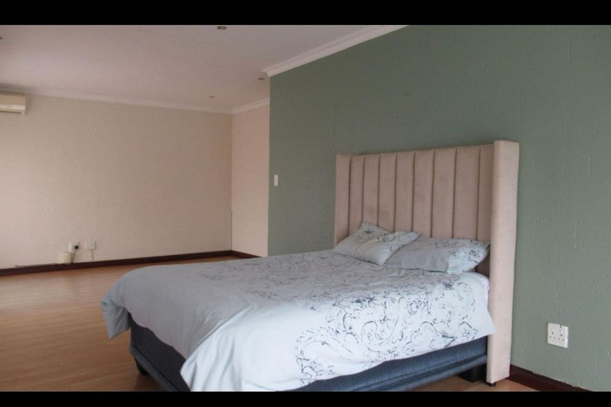 Spacious bedroom featuring laminate flooring, recessed lighting, and an integrated air conditioning unit, with a neutral and green accent wall finish.