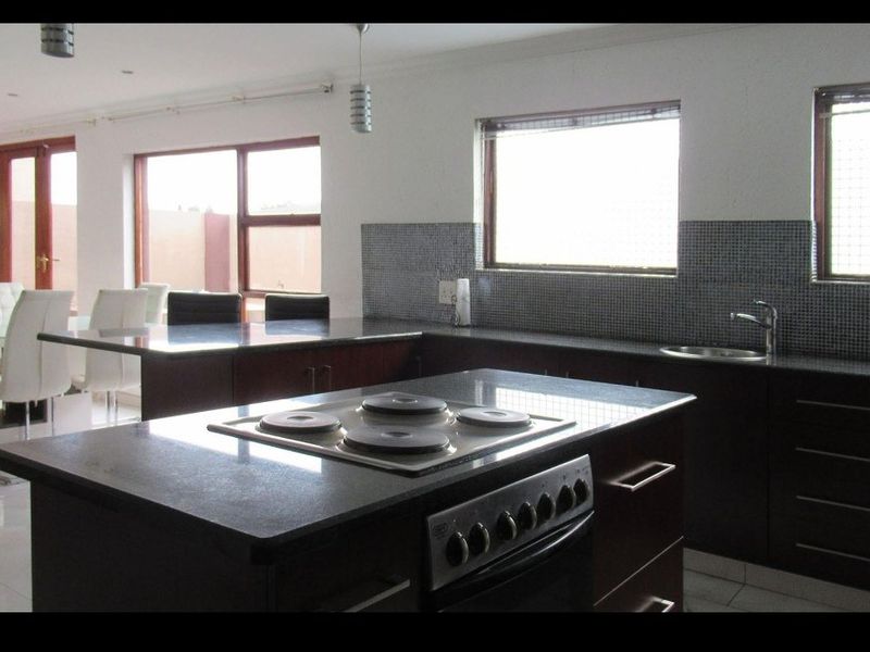 Open plan kitchen featuring a central island with built-in oven and hob, granite countertops, mosaic backsplash, and direct access to the dining area.