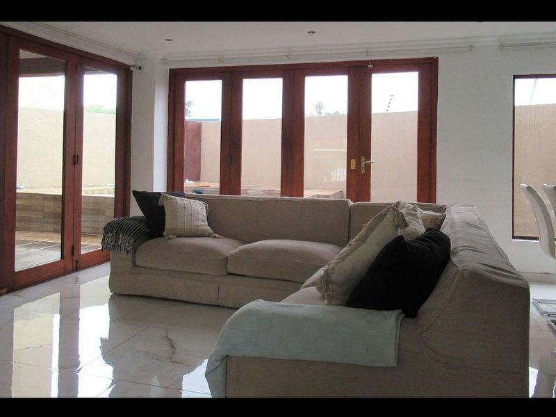Spacious open-plan living area featuring large format polished floor tiles and extensive wooden-framed folding doors providing seamless access to the outdoor patio.