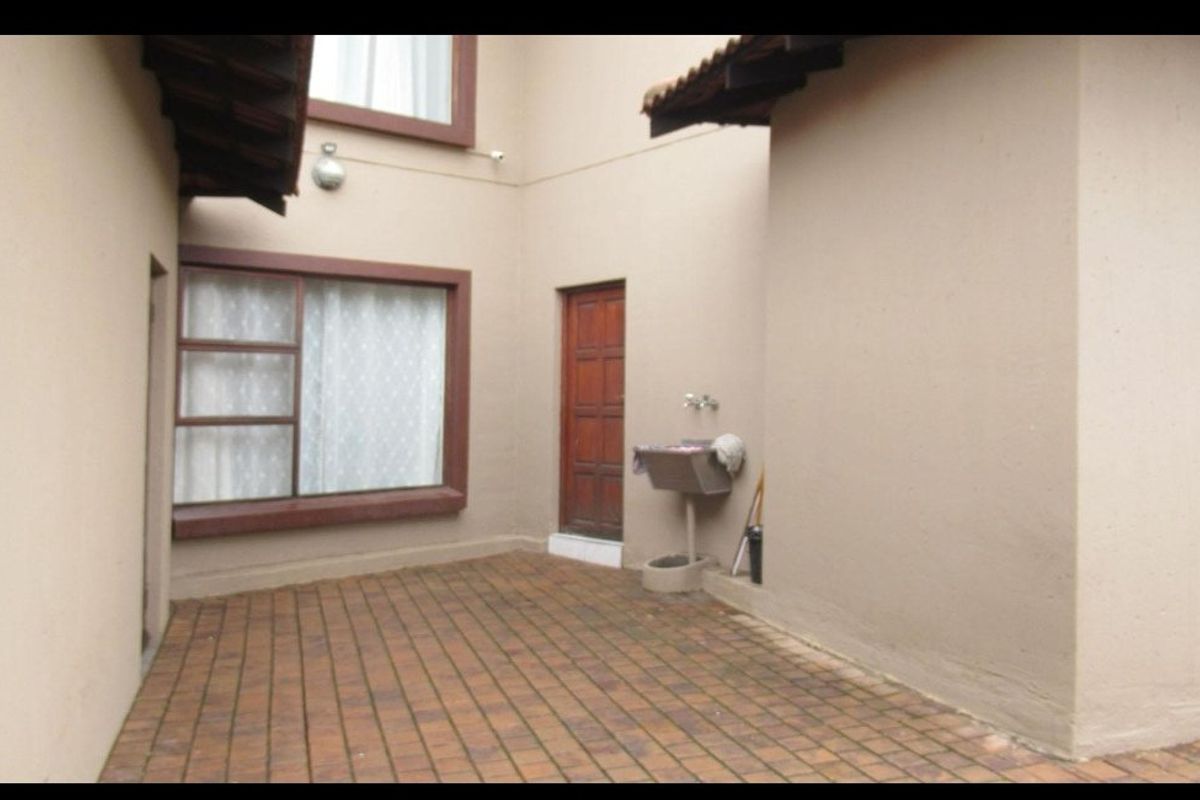 A paved rear courtyard area featuring a utility sink, timber door access, and exterior wall lighting.