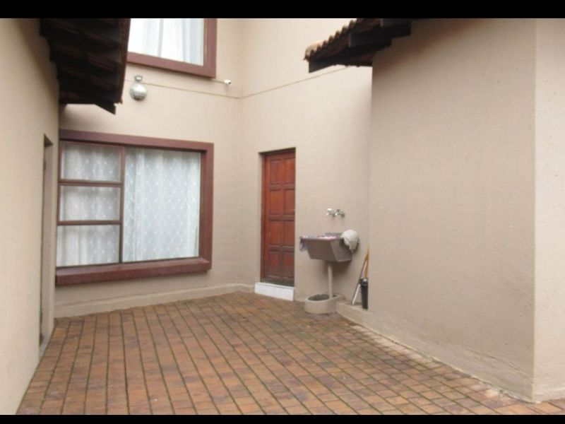 A paved rear courtyard area featuring a utility sink, timber door access, and exterior wall lighting.
