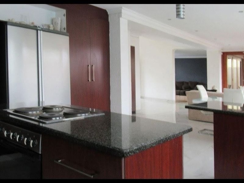 Open plan kitchen featuring dark wood cabinetry, granite countertops, and a built-in hob, flowing into the adjacent living and dining area.