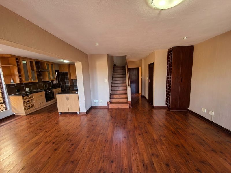 Spacious open-plan living area featuring laminate flooring, a functional kitchen with built-in appliances, and a central staircase leading to the upper level.