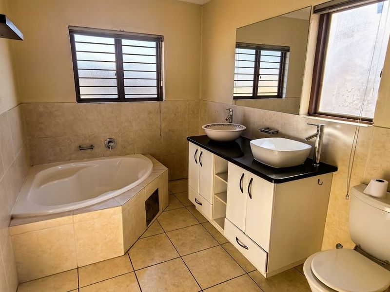 A spacious bathroom featuring a corner bathtub, double vanity with vessel sinks, and neutral wall and floor tiling.