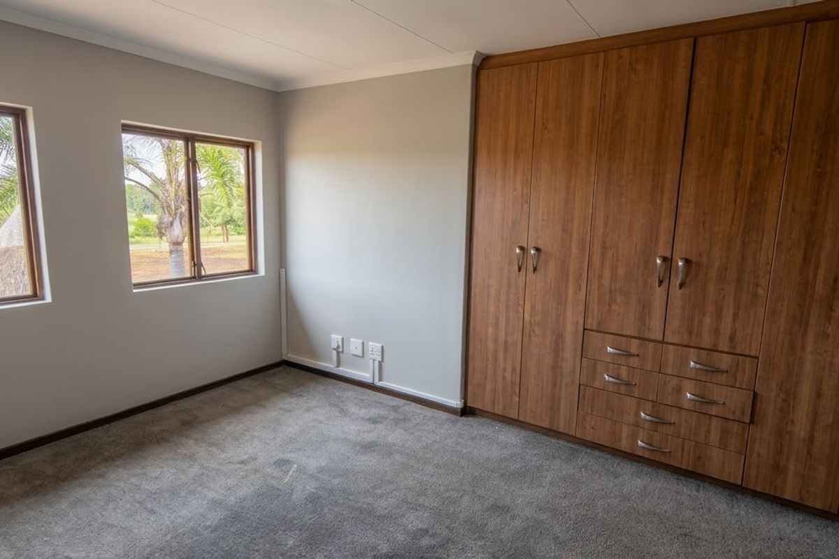 A bright and spacious bedroom featuring neutral walls, plush carpeting, and extensive built-in wooden cabinetry for ample storage.