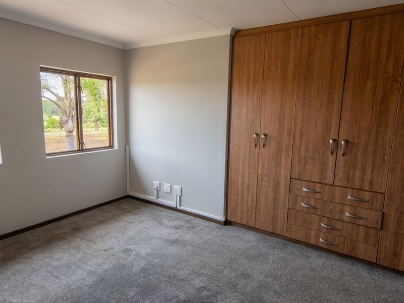 A bright and spacious bedroom featuring neutral walls, plush carpeting, and extensive built-in wooden cabinetry for ample storage.