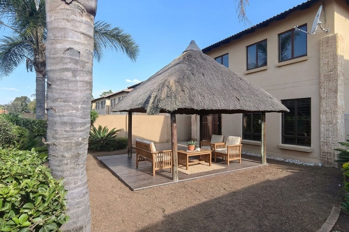 Rear garden area featuring a thatched gazebo structure on a tiled patio, set against the main house exterior with established landscaping.