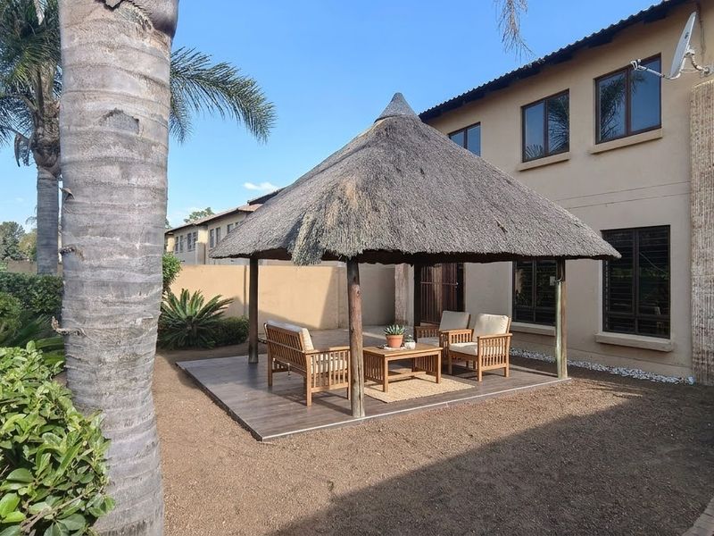 Rear garden area featuring a thatched gazebo structure on a tiled patio, set against the main house exterior with established landscaping.