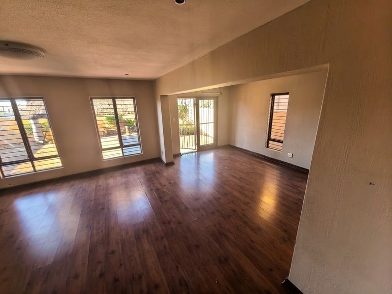 Spacious, empty living area featuring warm-toned laminate flooring, large windows with security bars, and a sliding door providing access to the exterior.