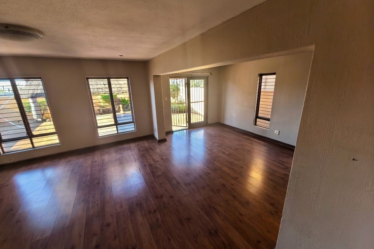 Spacious, empty living area featuring warm-toned laminate flooring, large aluminium-framed windows, and a sliding door providing access to the exterior.