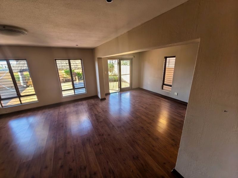 Spacious, empty living area featuring warm-toned laminate flooring, large aluminium-framed windows, and a sliding door providing access to the exterior.