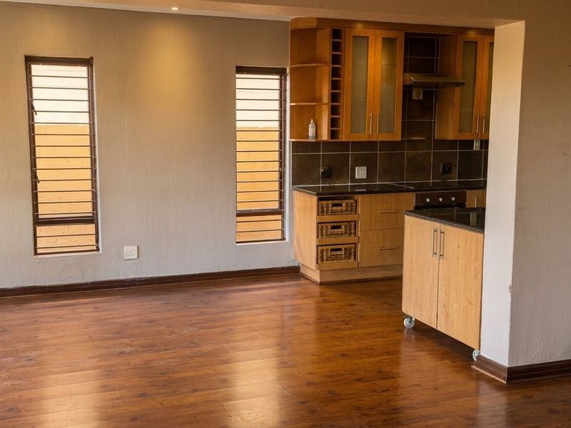 Open-plan living area featuring laminate flooring and a functional kitchen with built-in cabinetry, oven, and extractor fan.