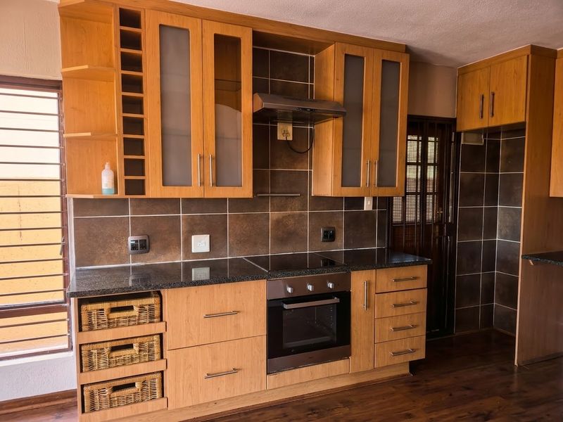 A well-maintained kitchen featuring light wood cabinetry, granite countertops, built-in oven and hob, and a dark tiled backsplash.