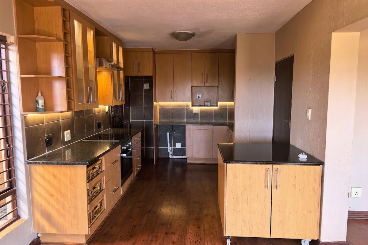 A functional kitchen featuring timber cabinetry, granite countertops, integrated appliances, and tiled backsplash, with an open layout and warm timber flooring.