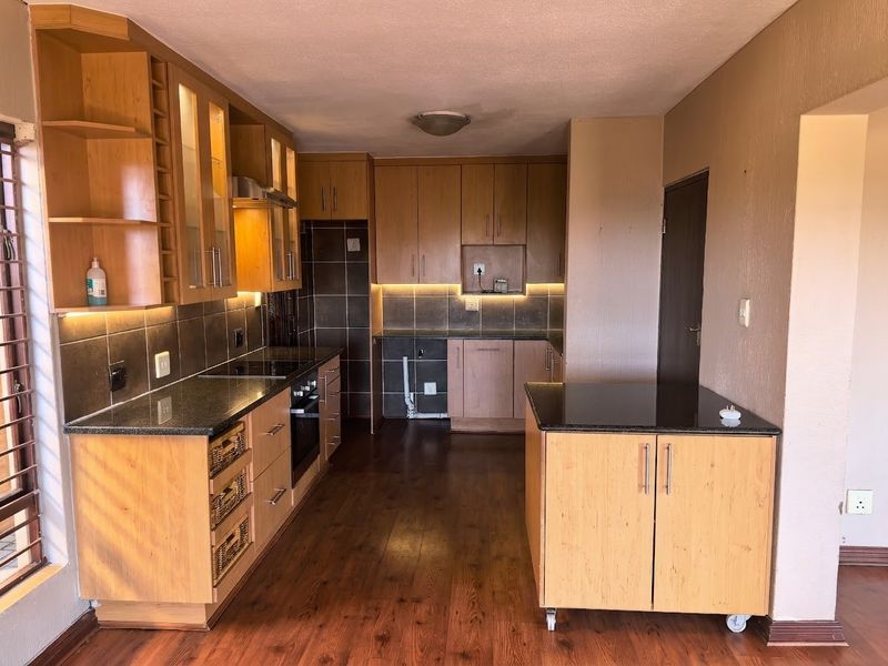 A functional kitchen featuring timber cabinetry, granite countertops, integrated appliances, and tiled backsplash, with an open layout and warm timber flooring.