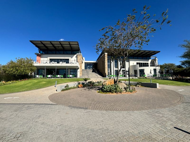 A well-maintained modern building exterior featuring stone accents, expansive balconies, and a paved driveway leading to a landscaped entrance.