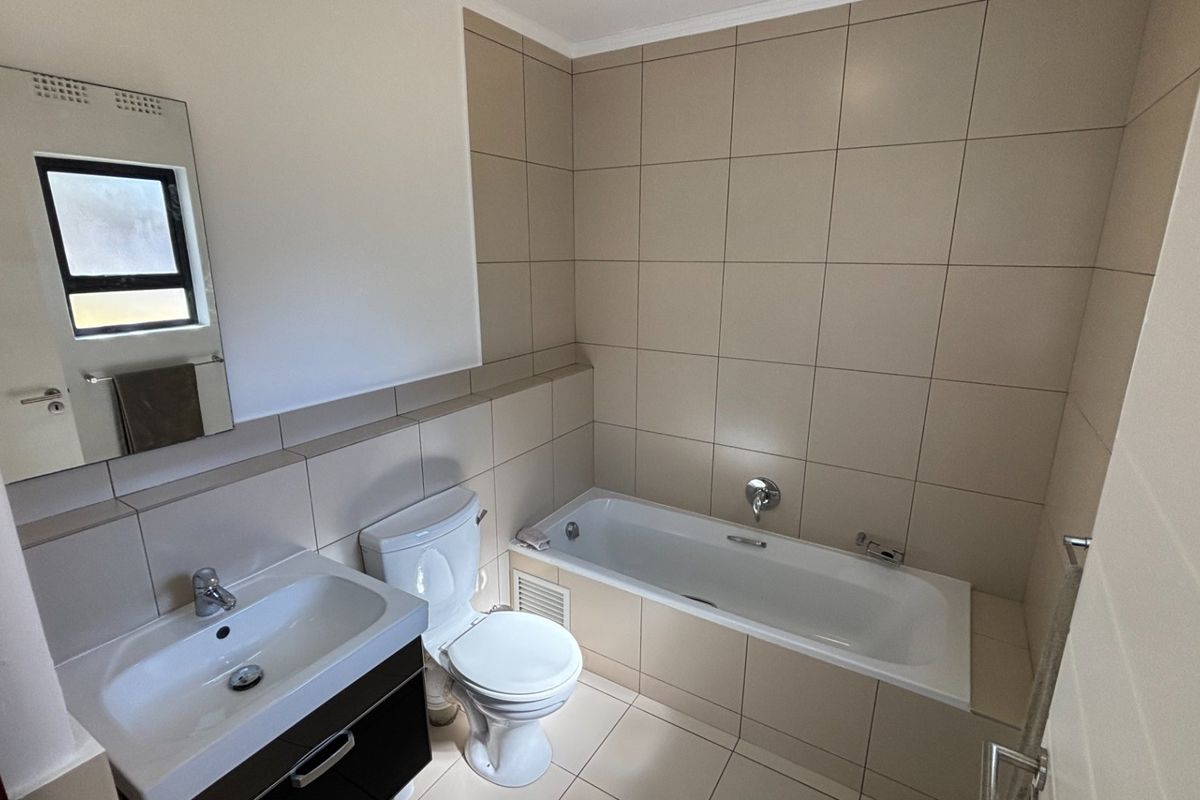 A clean and functional bathroom featuring neutral wall and floor tiling, a built-in vanity with basin, a standard toilet, and a bathtub.