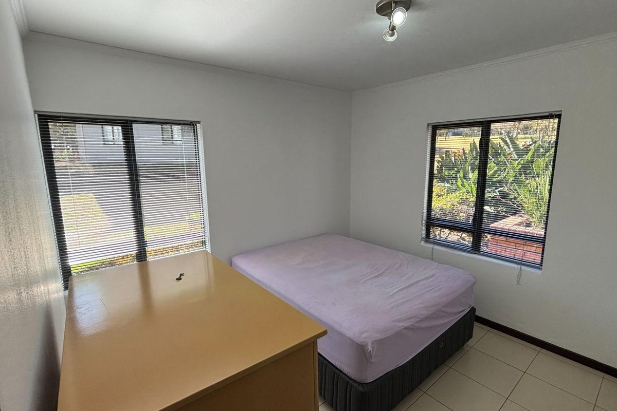 A functional bedroom featuring tiled flooring, dual aspect windows with venetian blinds, and neutral wall finishes, offering a bright and simple living space.