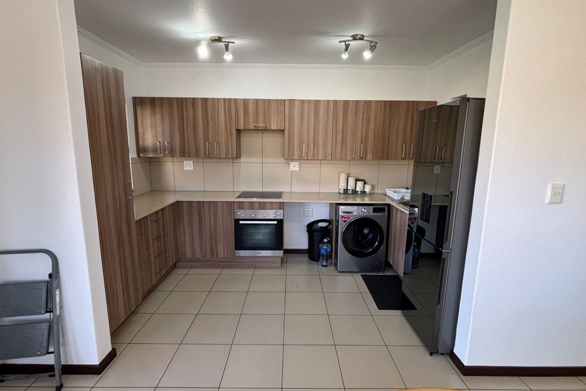 A functional kitchen featuring wood-finish cabinetry, laminate countertops, integrated oven and hob, and tiled flooring.