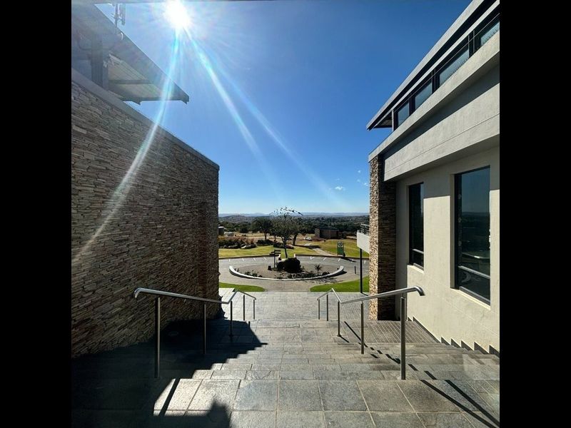 An impressive exterior entrance featuring a stone-paved staircase with stainless steel handrails, flanked by modern stone-clad walls and expansive windows overlooking the estate.