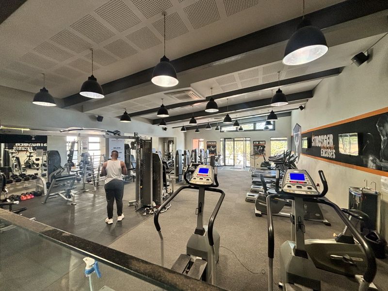 A well-equipped communal gym facility featuring rubber flooring, modern pendant lighting, and integrated air conditioning, providing a functional space for fitness activities.