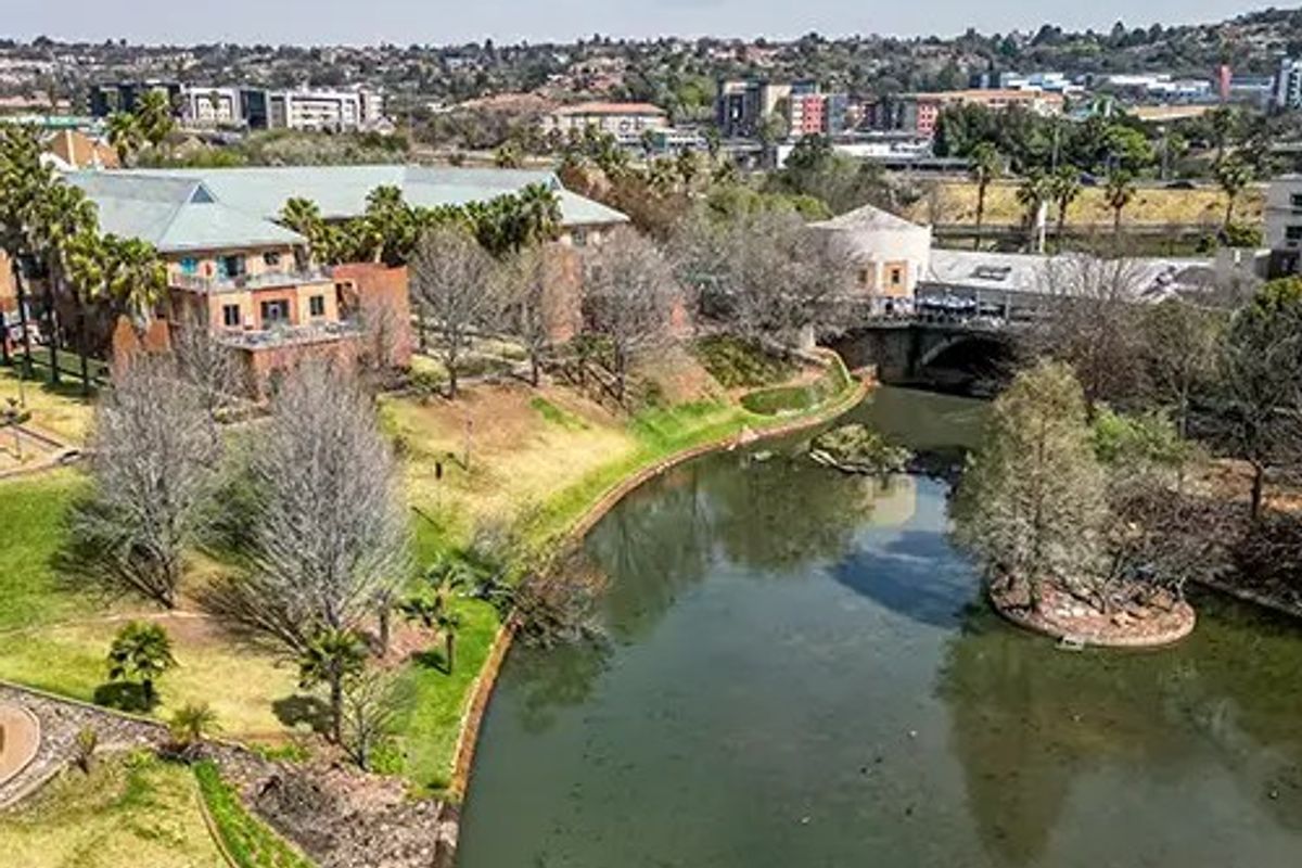 Aerial view of a commercial property complex situated alongside a river, featuring landscaped grounds and surrounding urban infrastructure.