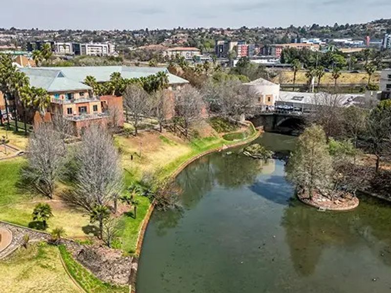 Aerial view of a commercial property complex situated alongside a river, featuring landscaped grounds and surrounding urban infrastructure.