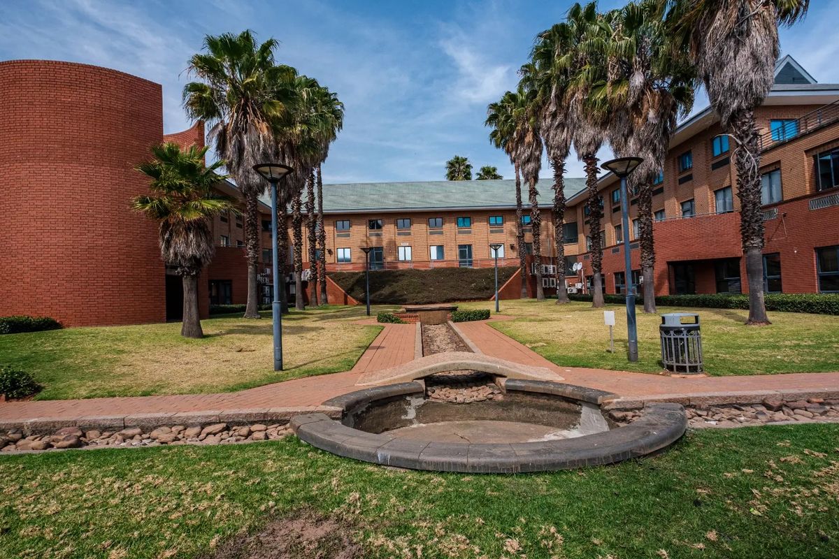 A view of the commercial property's rear courtyard featuring a brick facade, landscaped garden, paved walkways, and a central water feature.