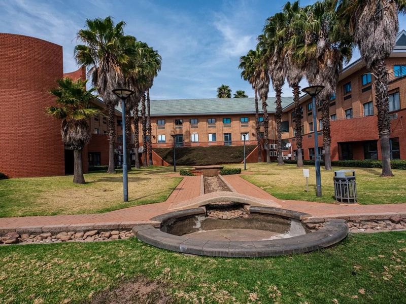 A view of the commercial property's rear courtyard featuring a brick facade, landscaped garden, paved walkways, and a central water feature.