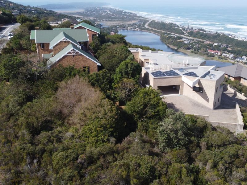 Aerial view of residential properties situated on a hillside, featuring modern architectural designs, solar panels, and scenic coastal and lagoon views.