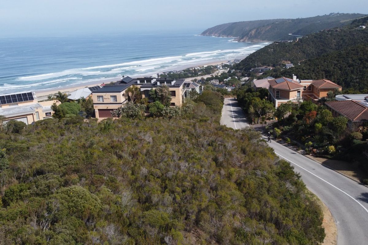 Aerial view of a vacant residential plot situated in a coastal neighborhood with direct road access and scenic ocean views.