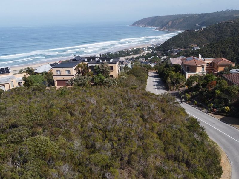 Aerial view of a vacant residential plot situated in a coastal neighborhood with direct road access and scenic ocean views.