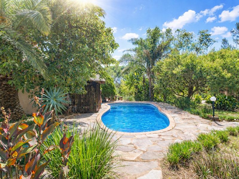 A private swimming pool set within a lush, landscaped garden featuring natural stone paving and mature trees.