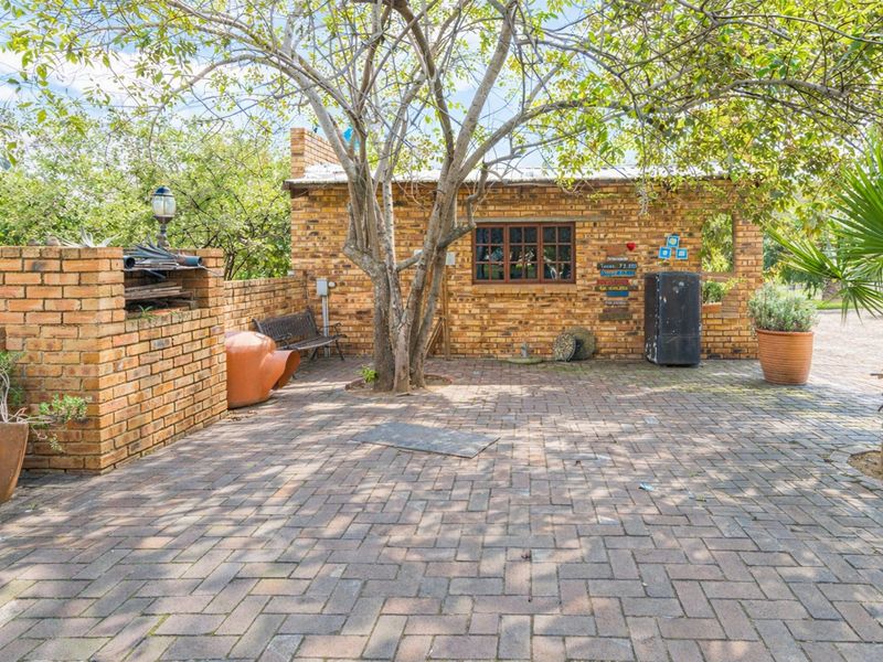 Outdoor patio area featuring brick paving and a built-in brick braai, set within a garden environment.