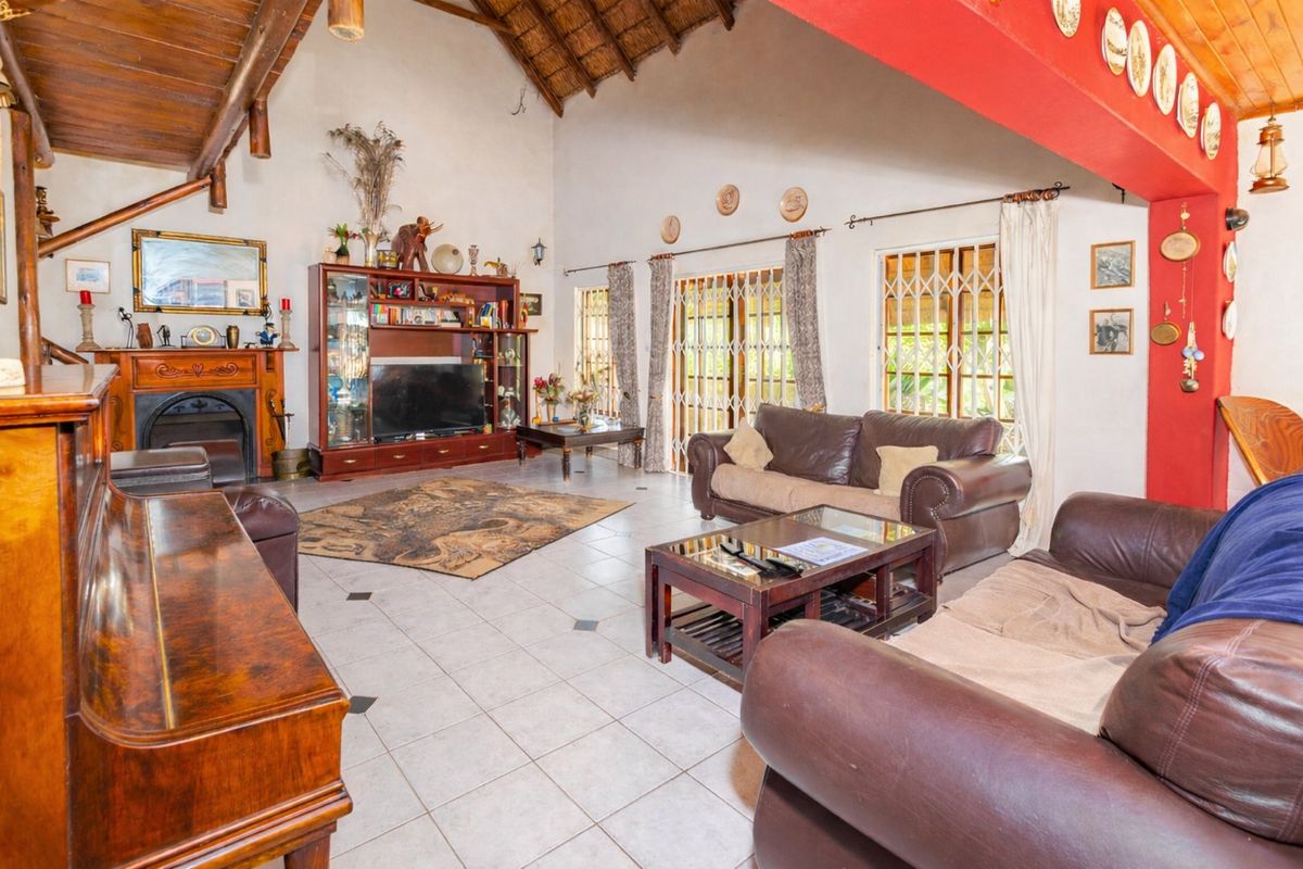 Spacious living room featuring a high thatched ceiling with exposed timber rafters, a traditional fireplace, and tiled flooring with direct access to the garden.
