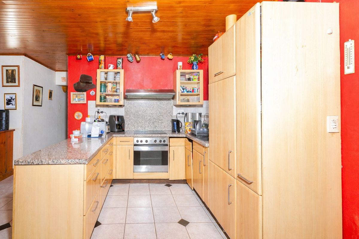 A functional kitchen featuring light wood cabinetry, granite countertops, stainless steel appliances, tiled flooring, and a distinctive timber-clad ceiling.