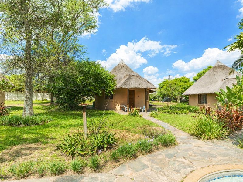 A view of traditional thatched-roof cottages set within a well-maintained garden, featuring stone pathways and access to a swimming pool area.