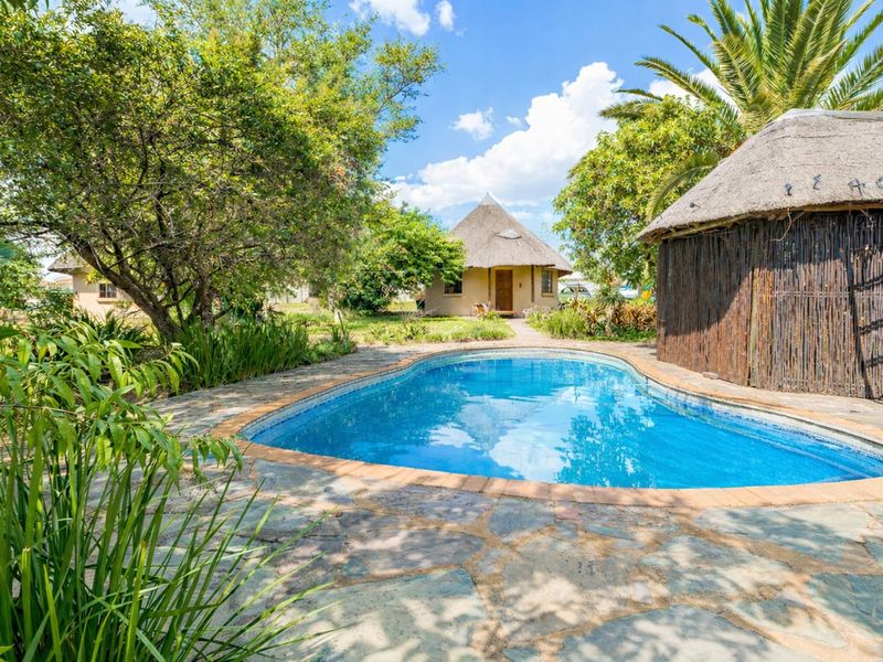 A well-maintained outdoor pool area featuring stone paving, a thatched lapa, and lush garden surroundings, perfect for relaxation and outdoor entertainment.