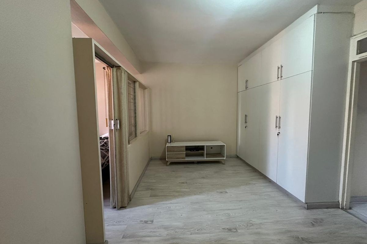 A bedroom featuring light-toned laminate flooring and extensive built-in white cupboards, offering ample storage space and a clean, neutral aesthetic.