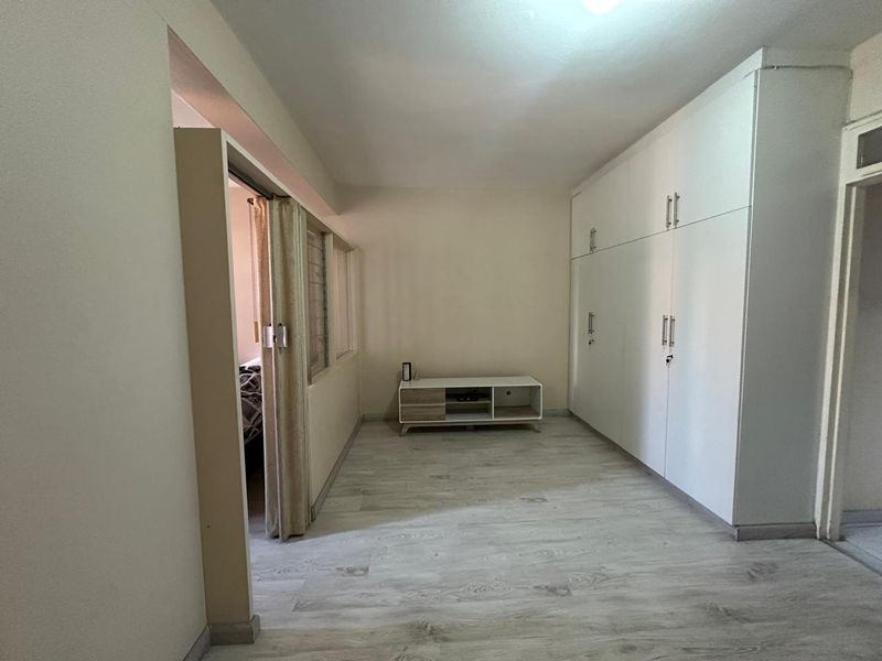 A bedroom featuring light-toned laminate flooring and extensive built-in white cupboards, offering ample storage space and a clean, neutral aesthetic.