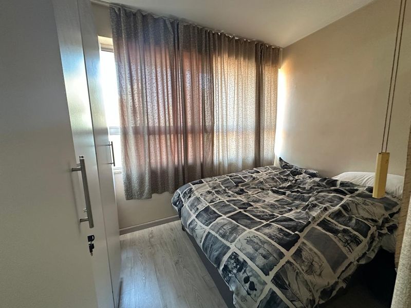 A compact bedroom featuring light-toned laminate flooring and a built-in wardrobe, offering a functional and neutral living space.