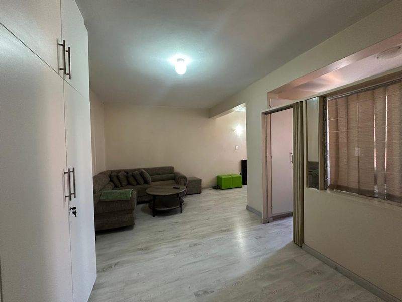 A living room featuring light-toned laminate flooring, built-in storage cupboards, and a sliding door leading to an adjacent space.