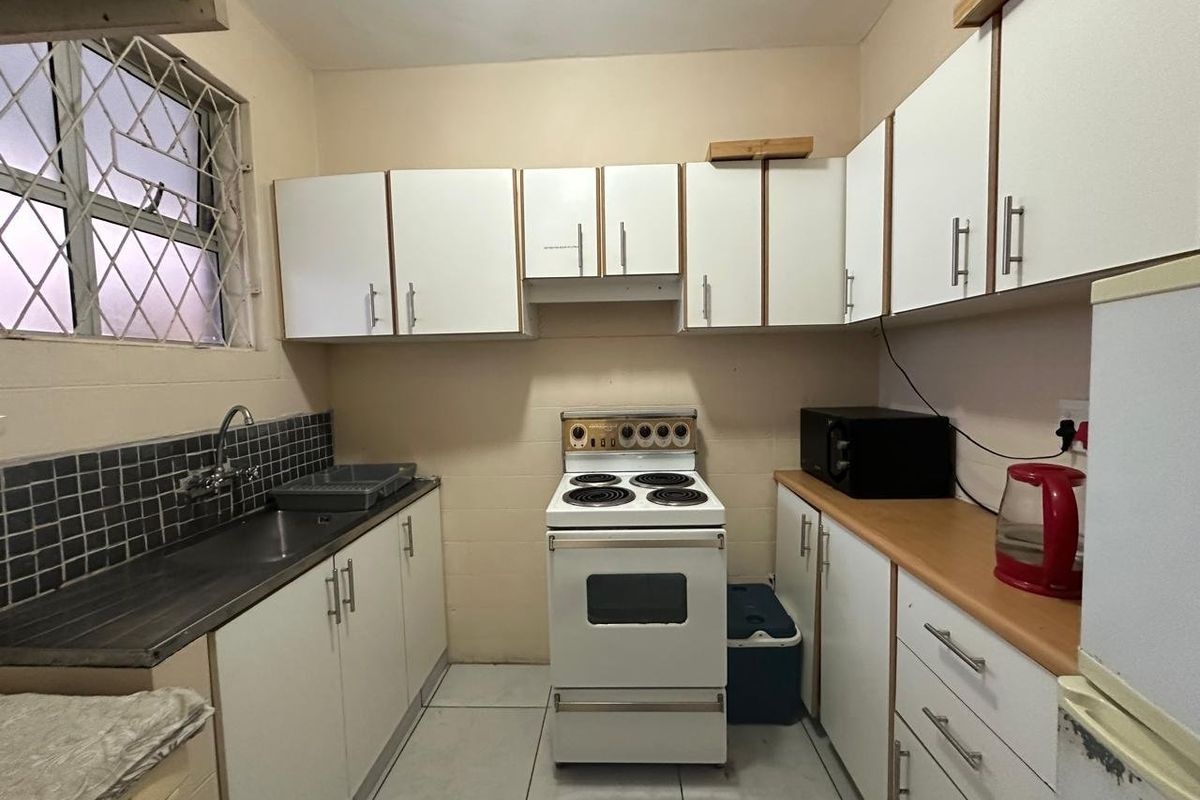 A functional kitchen featuring white cabinetry, laminate countertops, a tiled backsplash, and a freestanding stove, offering a practical layout for daily meal preparation.