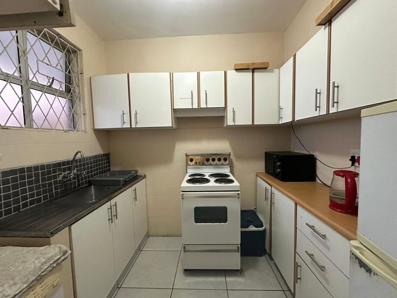 A functional kitchen featuring white cabinetry, laminate countertops, a tiled backsplash, and a freestanding stove, offering a practical layout for daily meal preparation.